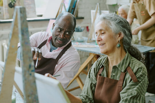High angle shot of African American husband pointing to canvas while giving advices to his beloved Caucasian wife