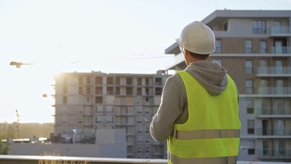Man constructive engineer with white hard hat and safety vest is using a tablet computer while...