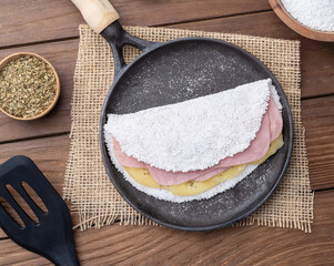 Traditional brazilian cheese and ham stuffed tapioca on a pan with ingredients