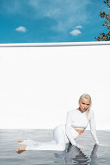 Beautiful fashion girl posing in white clothes in the studio while standing in the water