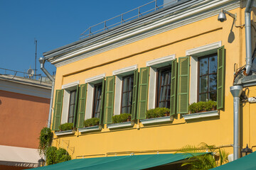 Vibrant colourful facade of house in summer. Yellow building with green shutters