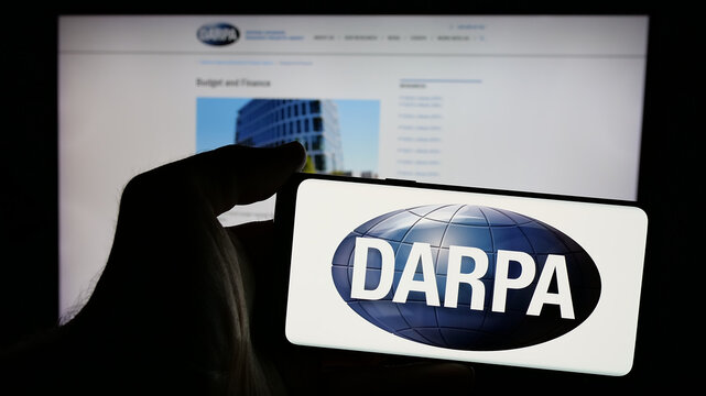 Stuttgart, Germany - 2024-10-10: Person holding mobile phone with logo of Defense Advanced Research Projects Agency (DARPA) on screen in front of web page. Focus on phone display.