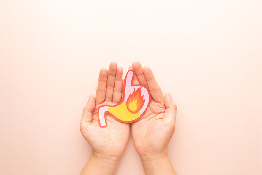 Human stomach burn with acid reflux and fire made from paper on hands. Gastroesophageal reflux disease (GERD) or heartburn symptoms. Gastrointestinal system disease and digestive problems.