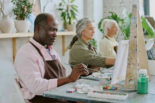 Small group of biracial retired people painting scenery on canvases during art therapy together - Powered by Adobe