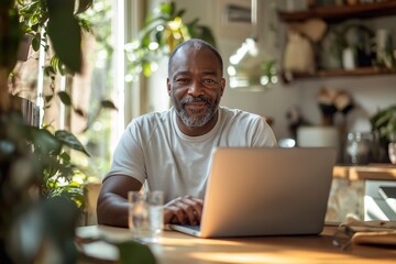 Obraz premium A man in his late forties smiles while working at a wooden desk in a cozy, plant-filled home office during daylight hours
