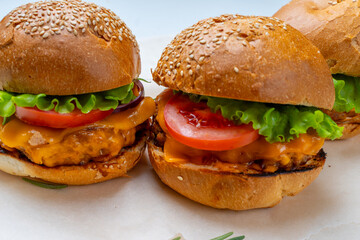 Juicy three burgers with beef patty, tomatoes, onions and lettuce on baking paper. on a light background