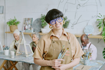 Portrait of young adult Caucasian drawing teacher holding paintbrushes and posing for photo