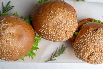 Juicy three burgers with beef patty, tomatoes, onions and lettuce on baking paper. on a light background
