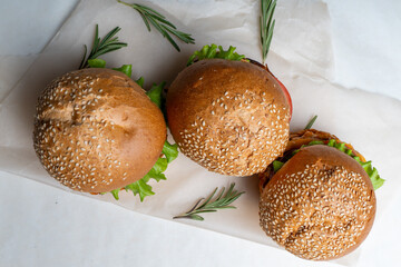 Juicy three burgers with beef patty, tomatoes, onions and lettuce on baking paper. on a light background