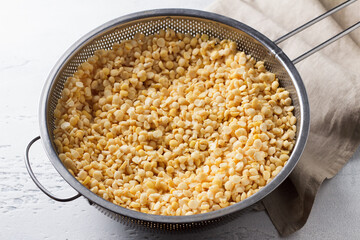 Yellow split soaked peas in a metal colander, stage of cooking, on a light gray background