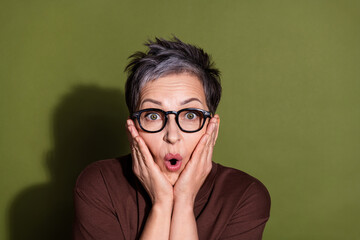 Photo portrait of gray hair beautiful cheerful pensioner grandmother in brown t shirt touching cheeks amazed isolated on khaki color background