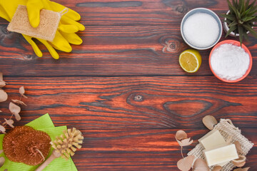 Top view zero waste eco friendly cleaning concept: baking soda, lemon, soap, with yellow cleaning gloves and brushes on a wooden background