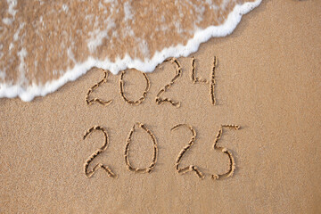 Fototapeta premium 2024, 2025 years written on sandy beach sea. Wave washes away 2024. Happy New Year!