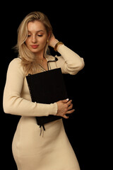 Portrait of a beautiful woman with a big black book on a black background. Isolate pretty blonde with book, with place for text