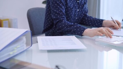 A female accountant with blue dotted blousy is using a laptop computer and calculator to calculate...