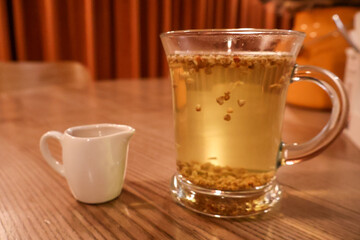 Glass Cup of Herbal Tea with Small Milk Jug on Wooden Table