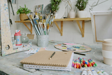 Medium close up of sketchbook, pastel chalks and different types of paints and brushes on old wooden table
