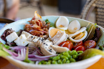 Un bowl de ensalada fresca con huevo duro, edamame, tomates cherry, bacon crujiente y otros...