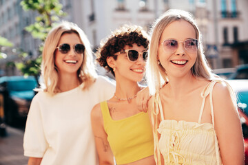 Three young beautiful smiling hipster female in trendy summer stylish clothes. Sexy carefree women posing in the street. Positive models having fun, hugging and going crazy, in sunny day, sunglasses