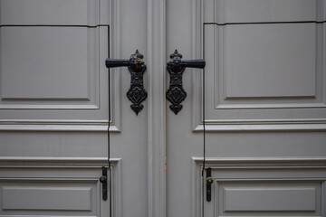 Vintage antique door handle on the old wooden door. Black door knob. Classic style with straight lines and decorative element on grey surface. Architecture in Italy. Details of double gray entrance
