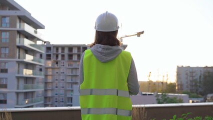 Female construction engineer is taking notes and writing on a clipboard while inspecting a construction site in the early morning at sunrise, back view