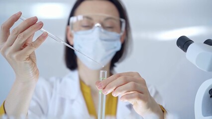 Woman with safety glasses and blue mask is working with lab tube