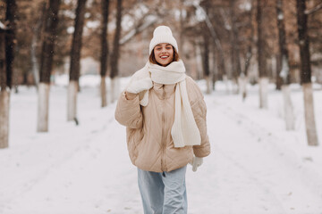 Obraz premium Happy smiling young woman portrait dressed coat scarf hat and mittens enjoys winter weather walking at snowy winter park