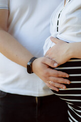 A pregnant woman in the arms of her husband. Summer sunny weather. A couple in love are hugging. Future parents. Young mom. Happy addition to the family. The concept of clothes for pregnant women.
