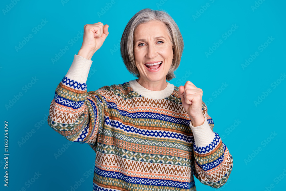 Wall mural Photo of overjoyed pensioner woman with white gray hair wear ornament sweater raising fists win gambling isolated on blue color background