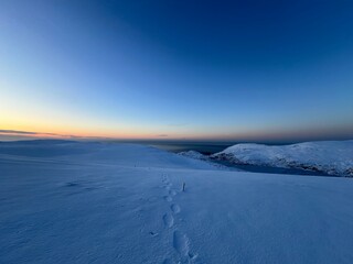 Seaside winter view. The photo captures a peaceful, snowy landscape at dusk while the sun sets down in the ocean in the Vest.