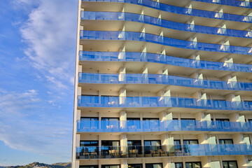 Modern apartment building with balconies and blue sky. Abstract architecture with glass panels. Perfect for modern design projects and presentations.