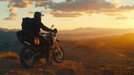The motorcyclist, fully protected in gear, stands tall on their motorcycle, looking out over rough, uneven ground toward the distant horizon, symbolizing the thrill of exploration