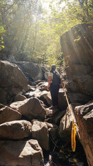  Young woman hiking in a green forest surrounded by big rocks, on a warm spring afternoon   