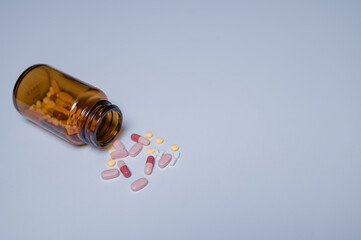 Spilled amber pill bottle various colorful tablets and capsules scattered on plain background, highlighting importance of careful medication storage and handling