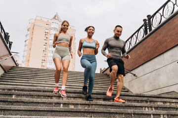 Diverse group of happy, smiling multinational sportspeople wearing sportwear run down the stairs