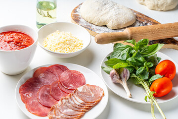 Ingredients for making Italian pizza: dough, tomato sauce, parmesan, tomatoes, basil, garlic, sausage on a white table. Real pizza recipe
