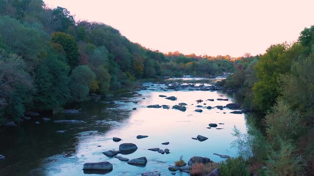 River with rapids. Beautiful fall nature by the river. River and rapids in the sunlight at sunset. Reflection of the sky and trees in the water. Aerial view.