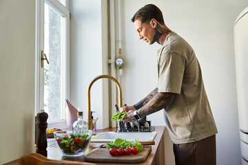A young man is preparing a salad, washing greens by the sink in a modern kitchen.