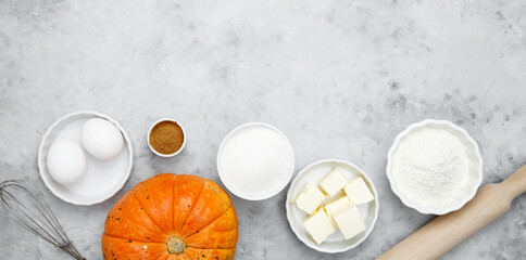 Baking ingredients including flour, butter, sugar, spices, eggs and pumpkin arranged on a gray background. Seasonal autumn baking
