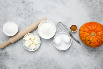 Baking ingredients including flour, butter, sugar, spices, eggs and pumpkin arranged on a gray background. Seasonal autumn baking