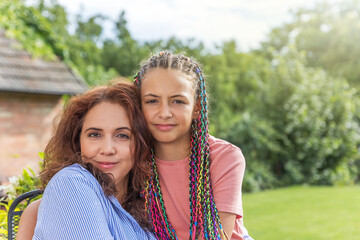 Fototapeta na wymiar Portrait of long haired mother and daughter looking at the camera posing at the garden. Horizontally. 