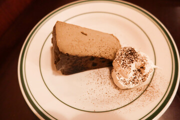 close up of earl grey tea hojicha tea flavour baked basque cheese ake with cream and chocolate power toppings on a whilte round plate