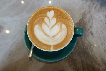 close up of milk coffee latte with heart and flower coffee art foam in a blue cup on a marble pattern table with a tea spoon