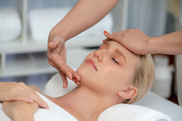 Fototapeta premium Caucasian woman enjoying relaxing anti-stress head massage and pampering facial beauty skin recreation leisure in dayspa modern light ambient at luxury resort or hotel spa salon. Quiescent