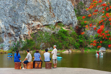 Fototapeta premium Back view of family relaxing together by the lake with blurred image of happy people enjoying pedal boats or water bikes in lagoon with beautiful canyon in background. Happy family holidays outdoors.