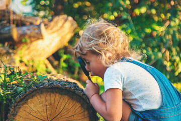 A child looks through a magnifying glass in nature. Selective focus.