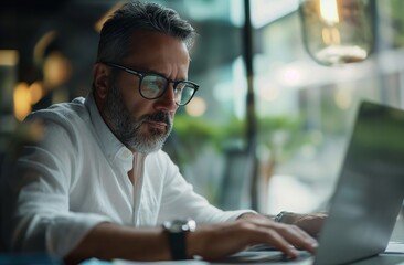 mature man with glasses working on a laptop.