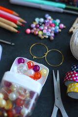 Colorful beads, coloring pencils, glitter, needles, string, hoop, tape and scissors on dark...