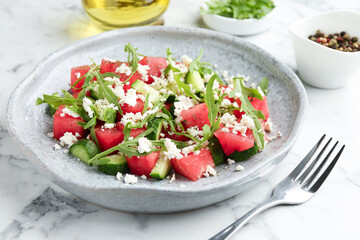 Delicious watermelon salad with feta cheese, cucumber and arugula served on white marble table, closeup