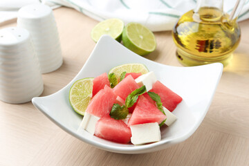 Tasty salad with watermelon, feta cheese, lime and mint on wooden table